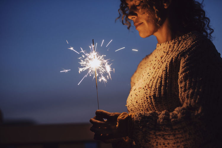 Woman holding illuminated fireworks against sky at night