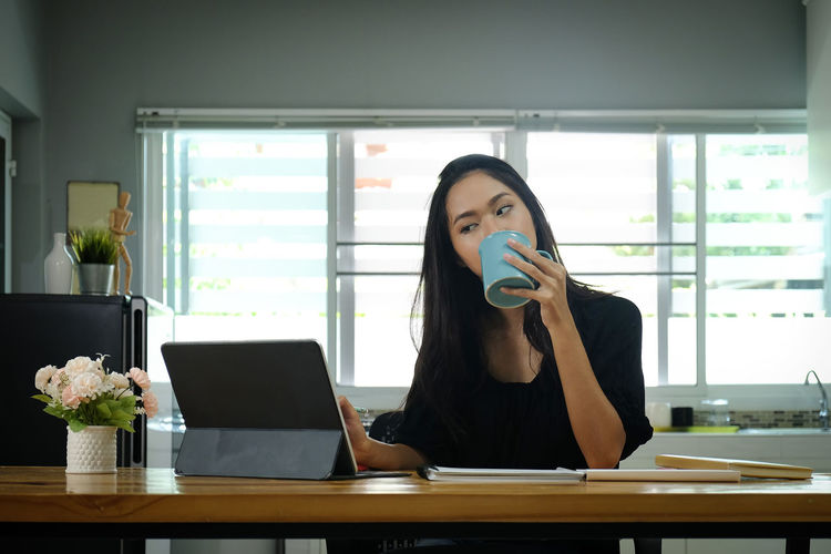 Businesswoman drinking coffee while looking at laptop