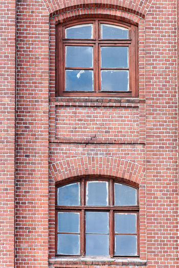 Two arched glass windows set in red brick wall. windows in brown wooden frames on red brick wall