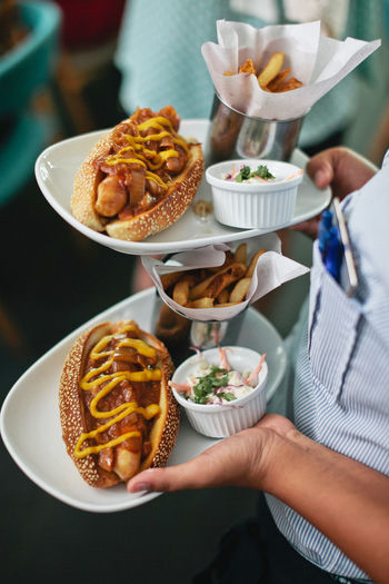 Midsection of waiter carrying hot dogs and french fries at restaurant