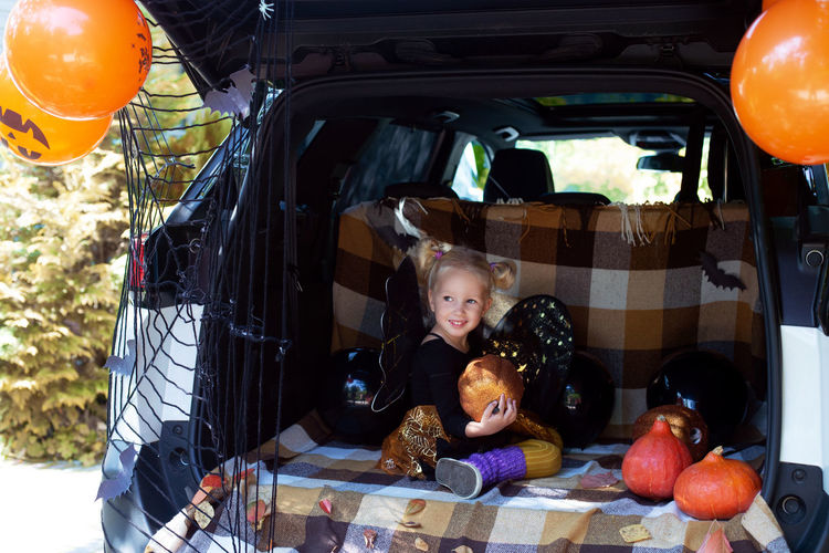 Cute girl looking away while sitting by halloween equipment in car