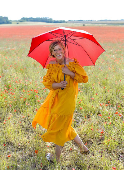 Happy woman with umbrella walking on grassy land