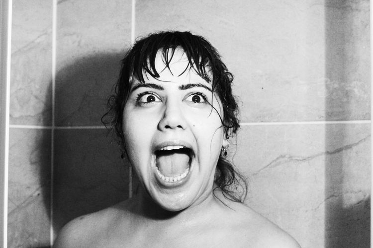 Shirtless young woman screaming against wall in bathroom