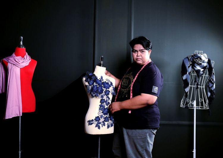 Portrait of designer holding mannequin while standing against wall