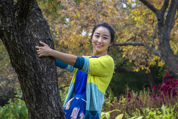 Portrait of a smiling young woman standing by tree
