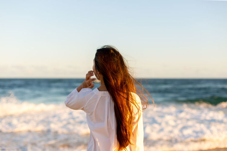 Rear view of woman standing at beach against clear sky