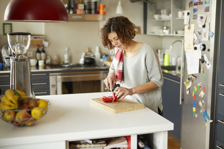 Mature woman cutting tomato in kitchen