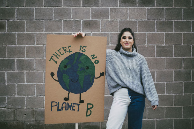 Portrait of smiling female activist standing by planet earth poster against wall