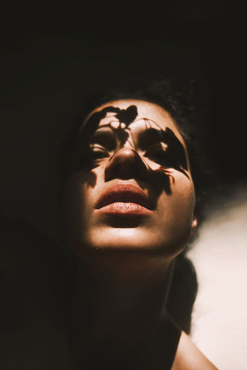 Young gentle woman with foliage shades on face looking at camera in light beam