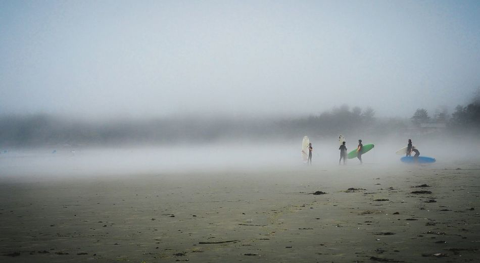 People with surfboards at beach during foggy weather