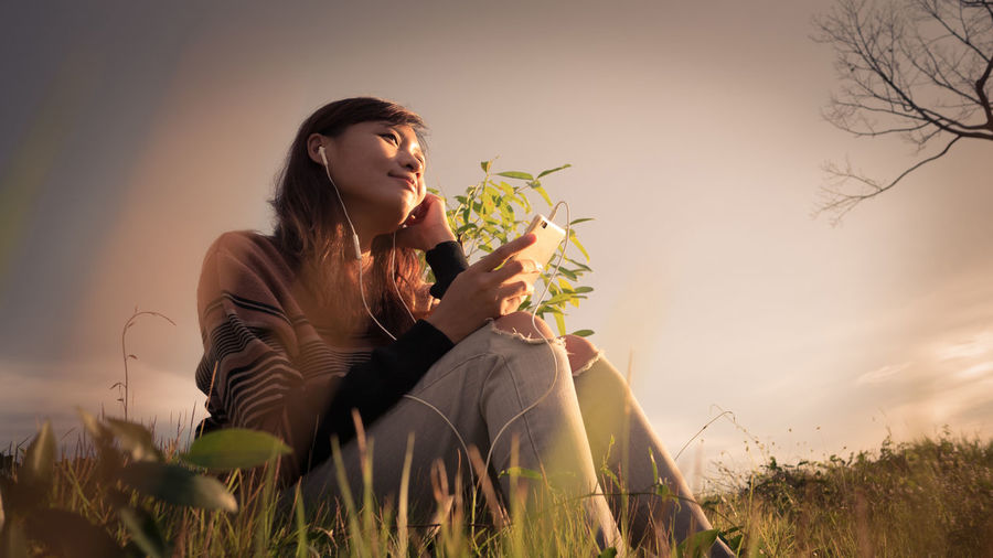 Young woman sitting on field against sky