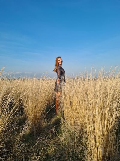 Young woman standing on field against sky