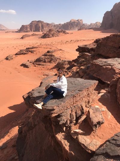 Woman sitting on rock formation at desert against sky