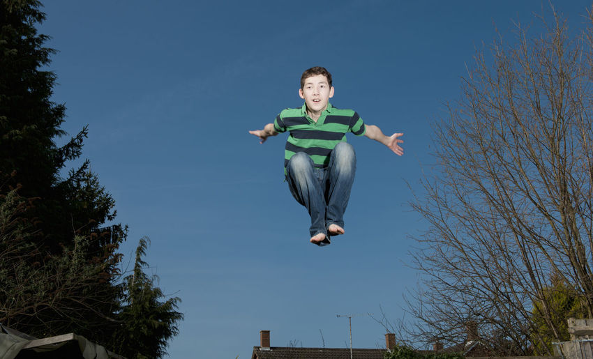 Low angle view of boy jumping against blue sky