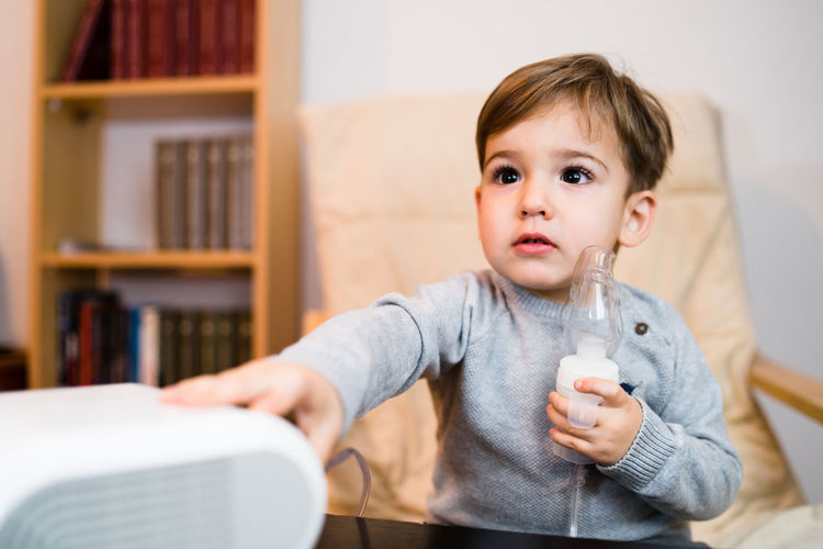 Cute boy holding oxygen mask at home