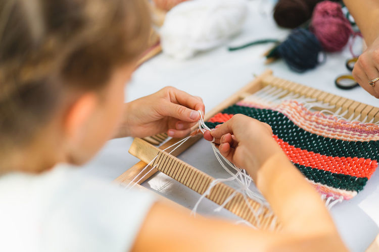 Girl weaving small rug with pattern at masterclass on weaving.