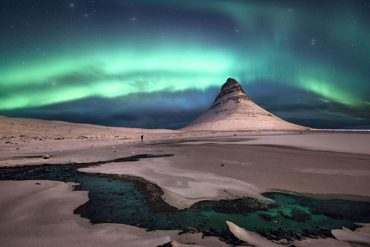 Scenic view of aurora borealis over snow covered landscape at night