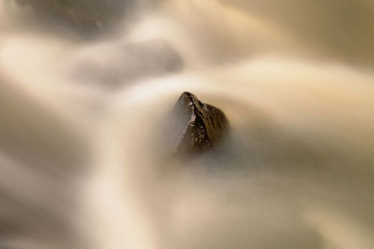 Slippery boulders in mountain stream. water blurred by long exposure, reflection in water level.