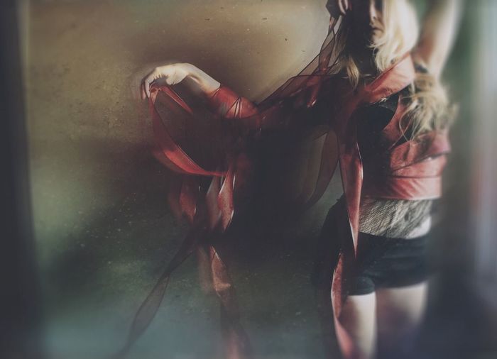 Blurred motion of woman wrapped in ribbon dancing against wall