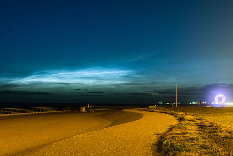 Road amidst illuminated field against blue sky at night