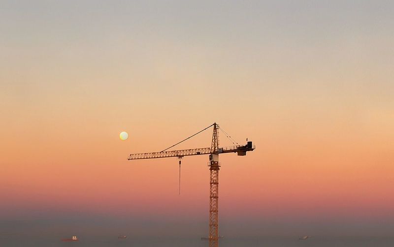 Cranes at construction site against sky during sunset