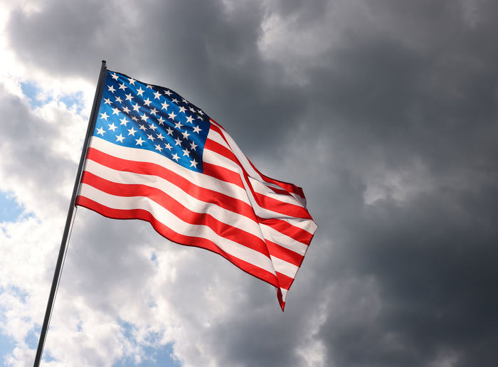 Us national flag flying and waving in the wind over gray stormy cloudy sky