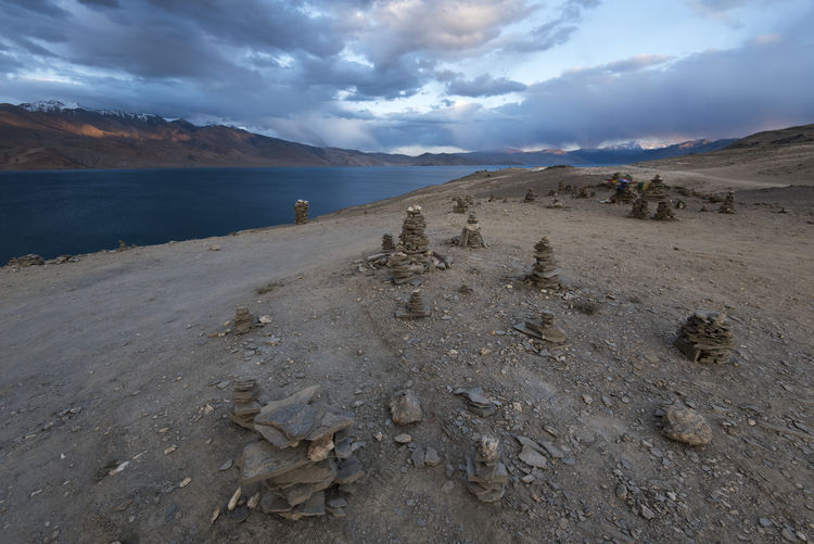 Stack of stones by lake against cloudy sky