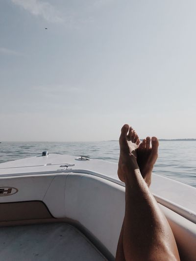Low section of person relaxing in boat on sea against sky