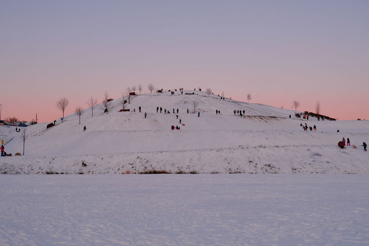 Group of people on snow covered land against sky during sunset