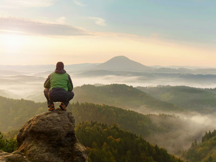 Man stay on rocky peak within daybreak and watch over misty landscape. beautiful autumn morning.