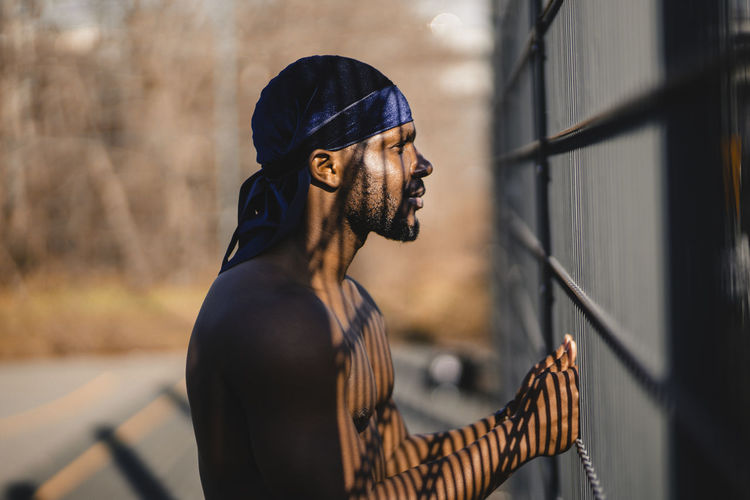 Shirtless man looking away while standing at railing during sunny day