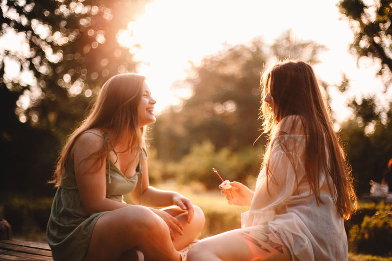 Happy girlfriends sitting in park during summer at sunset