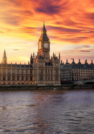 Big ben by thames river against cloudy sky during sunset