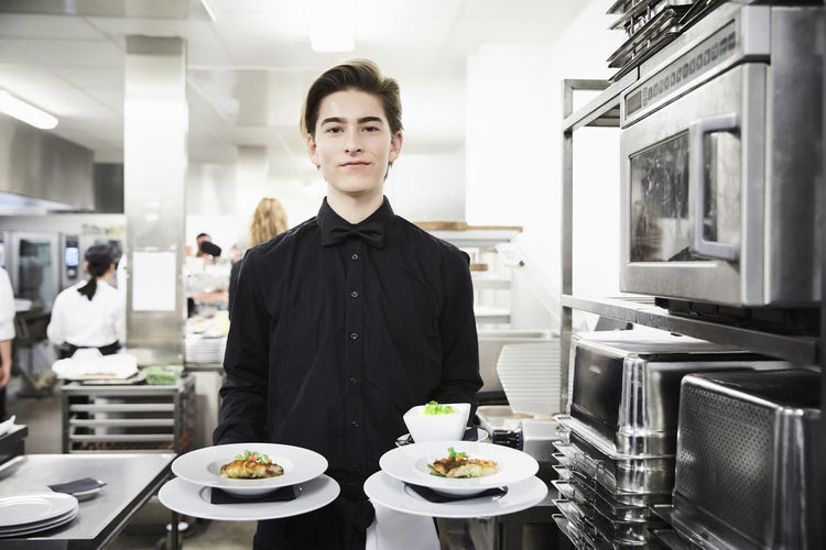 Portrait of confident waiter holding dishes in commercial kitchen