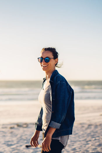 Portrait of smiling woman standing at beach against sky