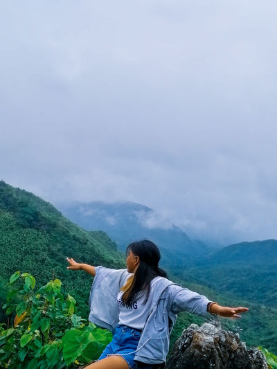 Rear view of woman sitting on mountain against sky