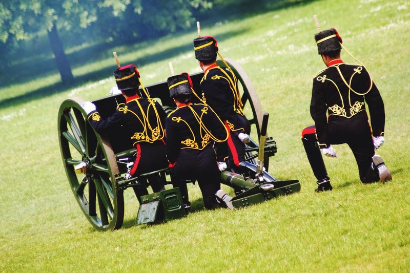 Rear view of army soldiers with metallic wheels on grassy field