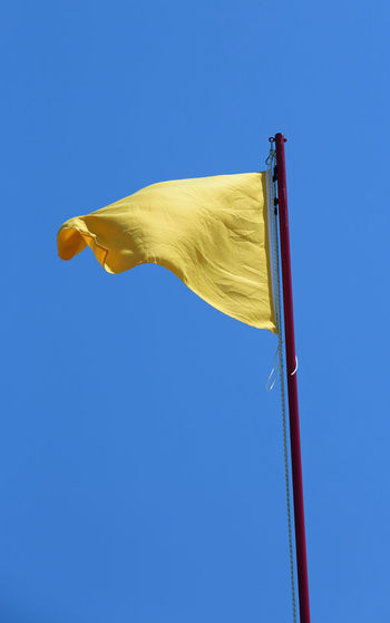 Big yellow flag symbol of danger of warning and the blue sky on background