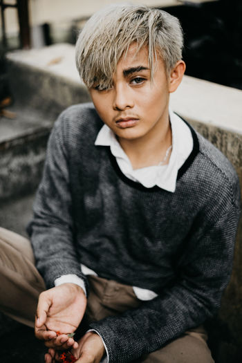 High angle portrait of young man sitting by retaining wall