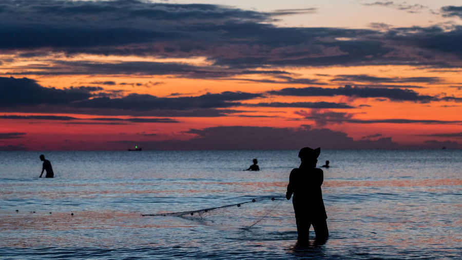 Silhouette man fishing on sea against sky during sunset
