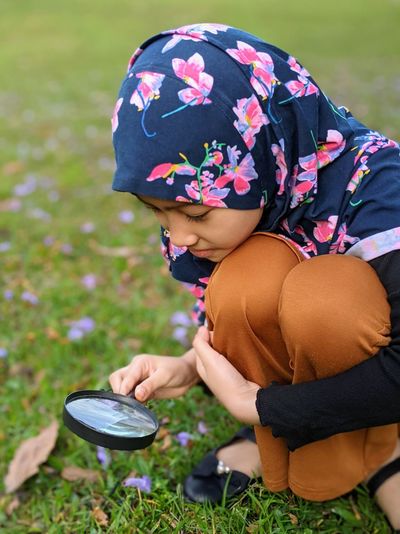 Midsection of girl holding magnifying glass on field