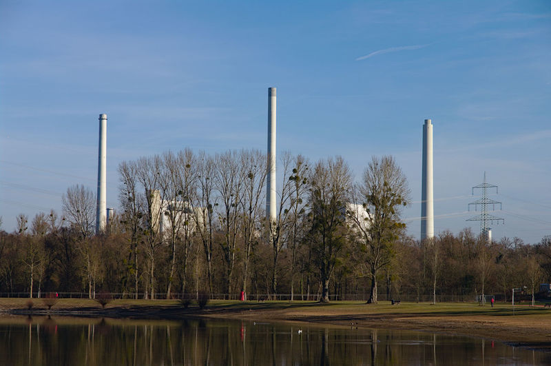 View of factory by lake against blue sky