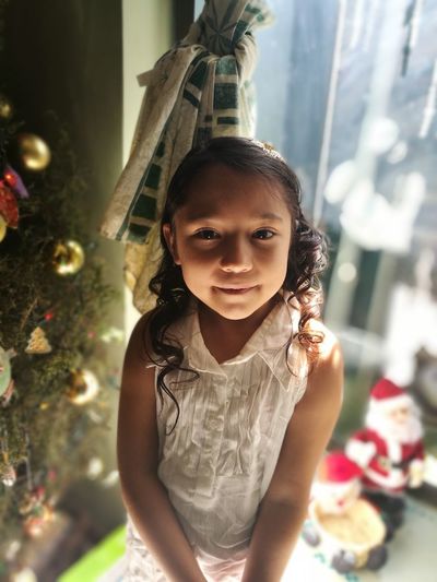 Close-up portrait of cute girl standing against christmas tree