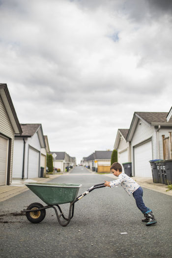 Young boy pushing wheelbarrow in back alley.