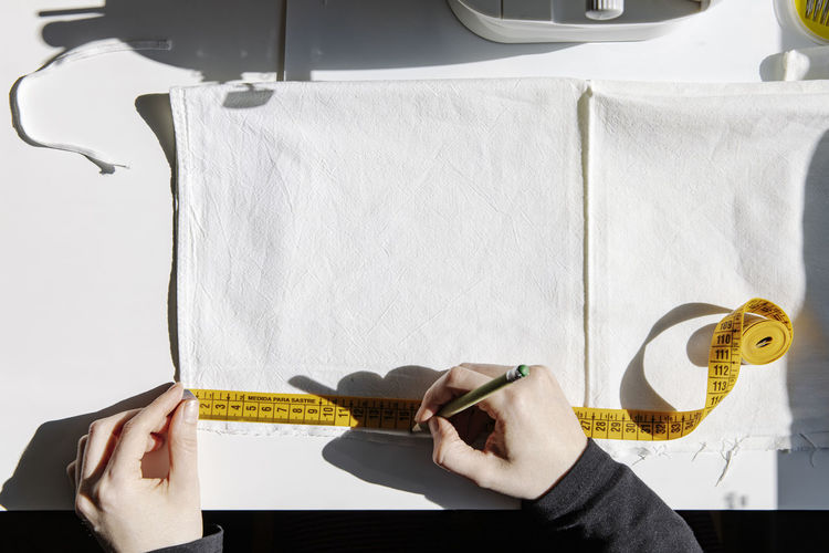 Overhead shot of tailor measuring fabric with a tape, in a sewing spot