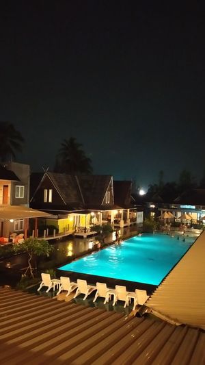 Swimming pool by illuminated building against sky at night