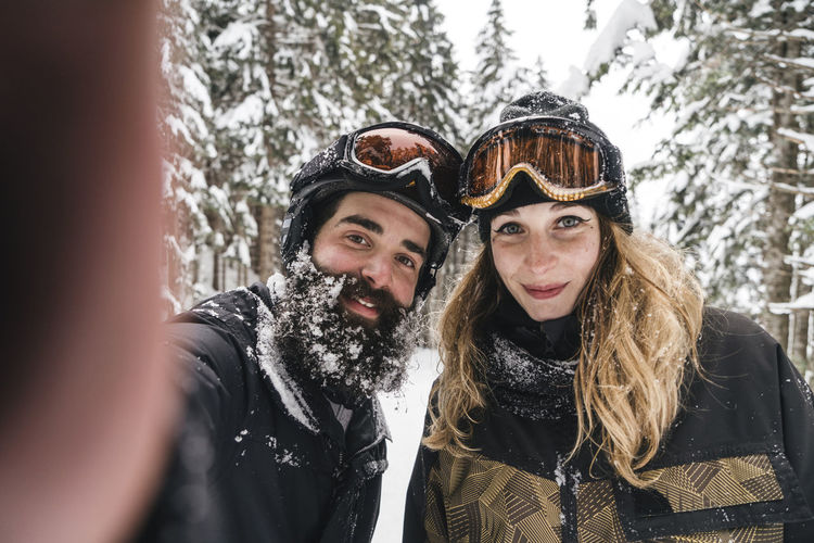 Selfie of smiling couple in skiwear in winter forest