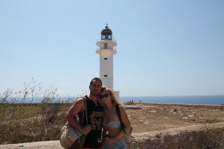 Portrait of couple with lighthouse in background against clear blue sky