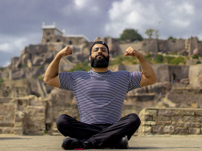 Portrait of bearded man flexing muscles while sitting against mountain