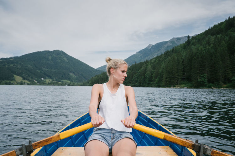 Woman rowing boat in lake against mountains